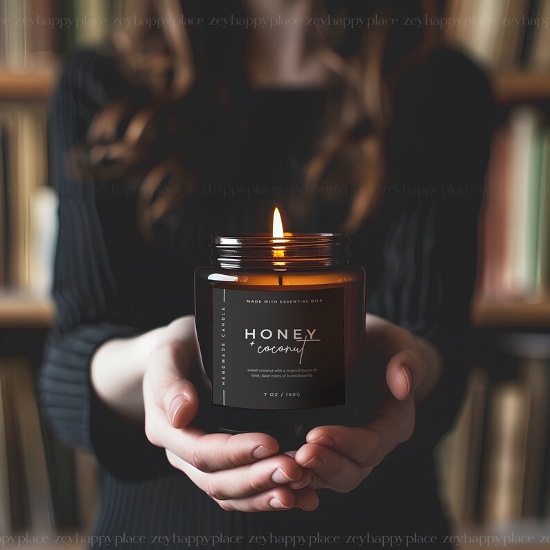 Pu&ograve; includere: Una candela di vetro marrone con un'etichetta nera che recita "HANDMADE CANDLE" e "HONEY + coconut". L'etichetta riporta anche "MADE WITH ESSENTIAL OILS" e "7 OZ / 150C". La candela &egrave; accesa e la fiamma &egrave; visibile.