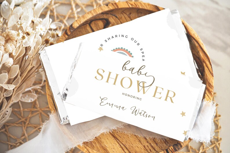 May include: A white card with gold lettering announcing a baby shower for Emma Watson. The card features a rainbow and stars.