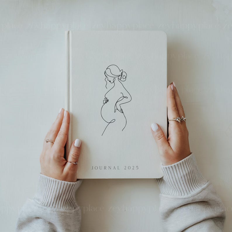 May include: A white journal with a line drawing of a pregnant woman on the cover. The journal has the text "JOURNAL 2025" printed on the bottom.