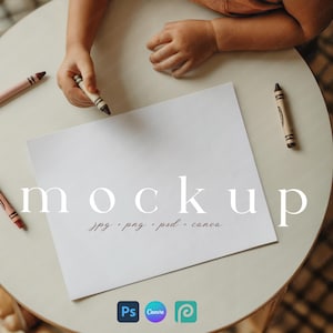 Op de afbeelding: Een witte papieren mockup met het woord "mockup" in een schreefletter. De tekst "jpg . png . psd . canva" staat onder het woord "mockup". Kleurpotloden en kinderhanden zijn zichtbaar. Het papier ligt op een lichtgekleurde ronde tafel.