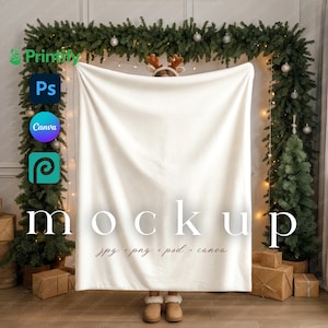 May include: A cream-colored blanket with the word "mockup" in large white letters. The blanket is held up in front of a Christmas-themed backdrop with a garland, Christmas trees, and wrapped gifts. The text "jpg + png + psd + canva" is also visible.