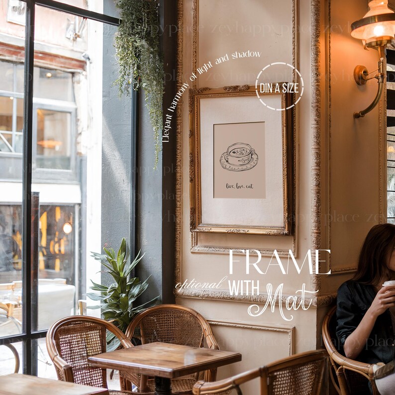 K&ouml;nnte beinhalten: Ein goldfarbener Rahmen mit einem wei&szlig;en Passepartout, der eine Schwarzwei&szlig;illustration einer Tasse Tee zeigt. Der Text "love, tea, eat" ist unter der Illustration gedruckt. Der Rahmen h&auml;ngt an einer Wand in einem Caf&eacute;-Ambiente.