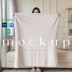 May include: A white throw blanket mockup with a person holding the blanket in front of their face. The blanket is on a white sofa with a brown cushion. The text "mockup" is written in white on the blanket. The text "jpg, png, psd, canva" is written in white below the word "mockup".