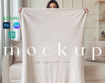 May include: A white throw blanket mockup with a person holding the blanket in front of their face. The blanket is on a white couch with a brown pillow. The text "mockup" is written in white on the blanket. The text "jpg, png, psd, canva" is written in white below the word "mockup".