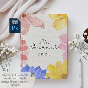 K&ouml;nnte beinhalten: Ein wei&szlig;er Journal-Umschlag mit dem Text "my daily Journal 2025" in Schwarz. Der Umschlag ist mit Aquarellblumen in den Farben Rosa, Gelb, Blau und Rot verziert.