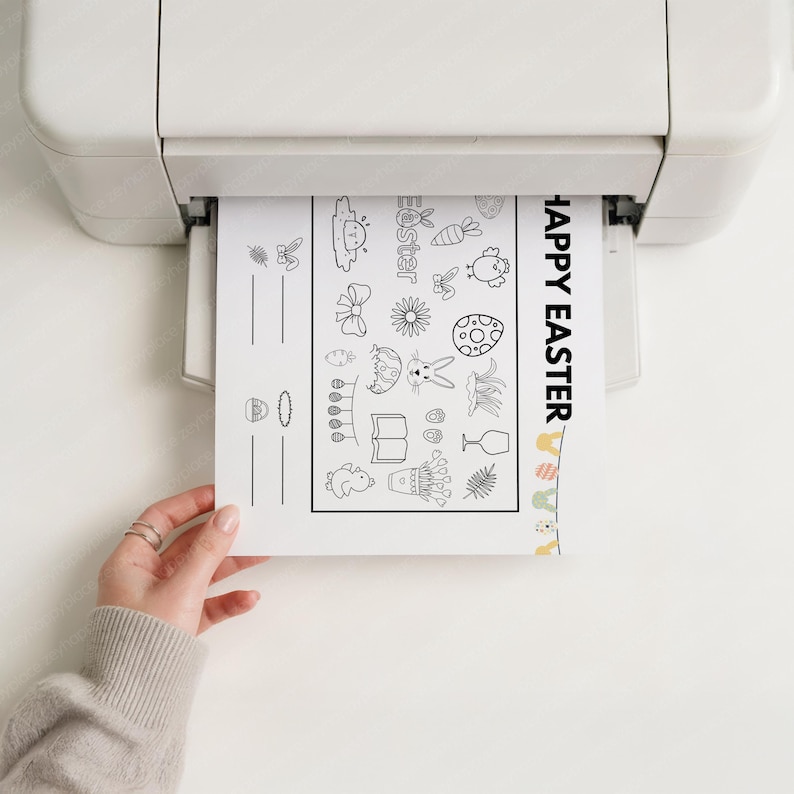 May include: A printer is outputting a black and white Easter-themed coloring page. The page features various Easter-related illustrations, including eggs, bunnies, and flowers, with the words "Happy Easter" printed vertically on the right side.