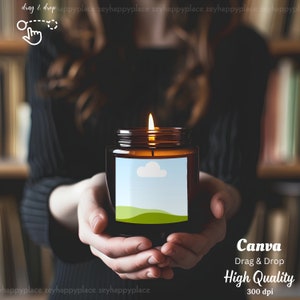 Pu&ograve; includere: Un barattolo di vetro marrone con una candela e un'etichetta bianca che presenta un paesaggio verde e una nuvola blu. La candela &egrave; accesa e la fiamma &egrave; visibile. Il testo "Canva Drag & Drop High Quality 300 dpi" &egrave; stampato sotto il barattolo della candela.