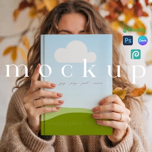 May include: A mockup book with a blue sky and cloud design, held by a person. The book has a green landscape at the bottom. The word "mockup" is displayed on the book. The book is for jpg, png, psd, and canva.
