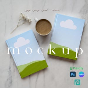 May include: Two hardcover books with blue sky and cloud designs, green landscape bottoms, and the word "mockup" in white. A white mug of coffee and a sprig of white flowers are also present.