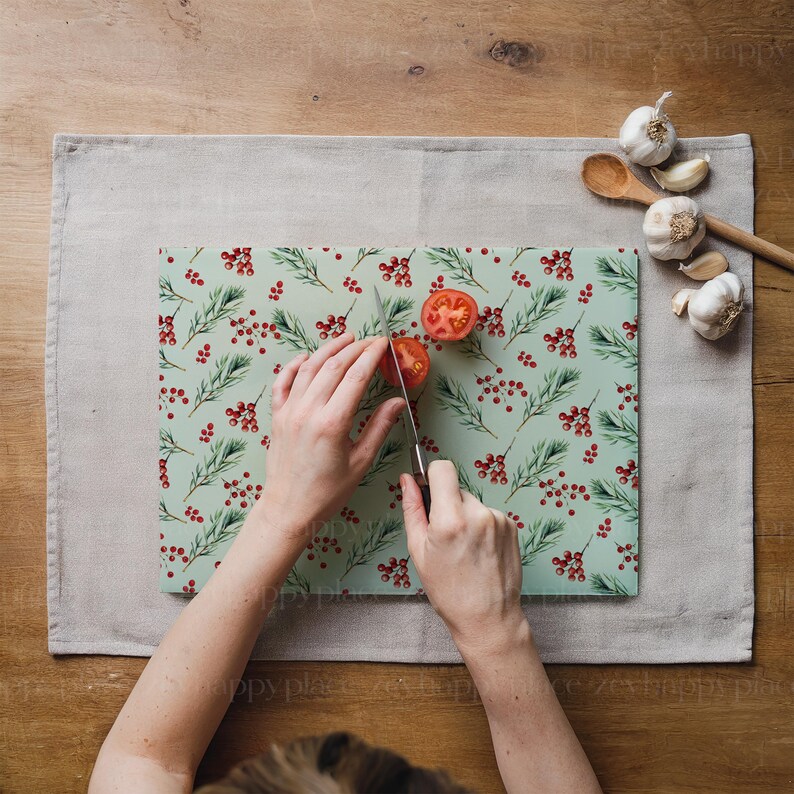 Op de afbeelding: Een persoon snijdt een tomaat op een groen en rood gepatroneerd snijplank. De plank heeft een kerstthema met kleine rode bessen en groene bladeren.