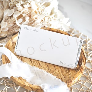 Puede incluir: Una maqueta de barra de chocolate blanco con el texto "PSD + JPG" y "zey zeyhappyplace" en una bandeja de madera con cinta blanca y flores secas.