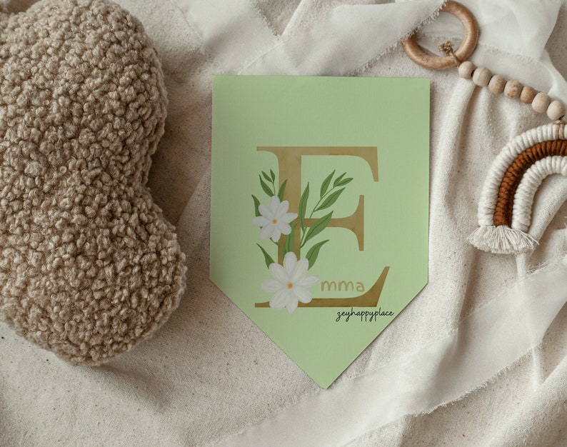 May include: A green and gold letter E with white flowers and green leaves. The letter is on a light green banner with the text "emma" and "greyhappyplace" in gold.