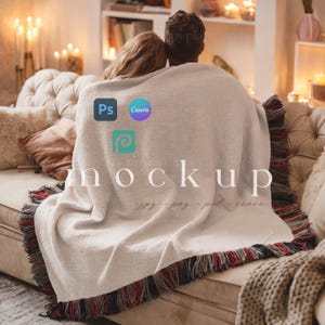 May include: A couple sits on a couch wrapped in a white blanket with a fringe border. The blanket has the words "mockup" and "jpg - png - psd - canva" printed on it. The blanket is a mockup for a design project.
