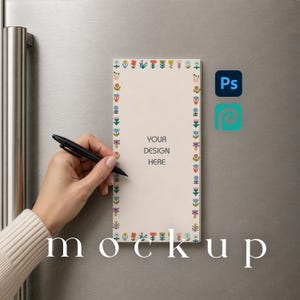 May include: A rectangular magnetic notepad with a cream-colored background and a colorful border of small stylized flowers. The center of the notepad features the text 'YOUR DESIGN HERE' in a dark gray font. A black pen is held against the notepad.