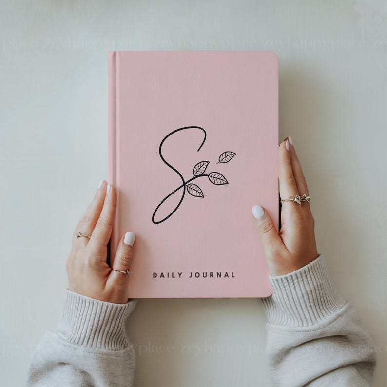 May include: A pink daily journal with a black floral design and the text "DAILY JOURNAL" on the cover.