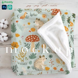 May include: A soft, white fleece blanket with a blue and green patterned fabric underneath. The fabric features a repeating pattern of mushrooms, hedgehogs, and leaves. The text "mockup" is printed on the fabric.