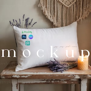 Könnte beinhalten: Weißes rechteckiges Kissen-Mockup mit dem Wort "Mockup" in großen weißen Buchstaben. Das Kissen liegt auf einem alten Holztisch mit Lavendel und einer brennenden Kerze. Die Logos von Printify, Photoshop, Canva und Etsy sind sichtbar.