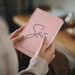 May include: A pink daily journal with a black floral design and the letter "S" on the cover.
