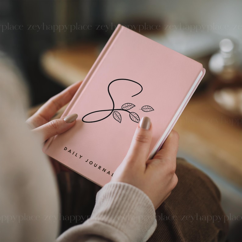 May include: A pink daily journal with a black floral design and the letter "S" on the cover.