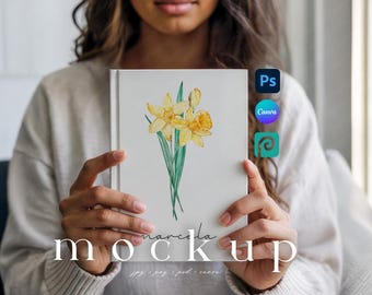 May include: A white book cover featuring a watercolor illustration of yellow daffodils with green stems and leaves. The word "marcela" is written in cursive, and the word "mockup" is below it in a bold font. The image also includes the logos for Photoshop, Canva, and another design tool.