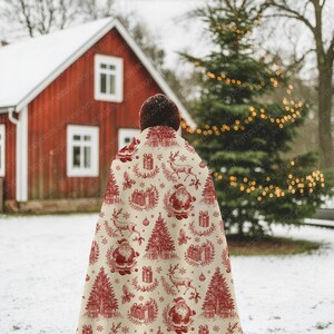 May include: A cream-colored Christmas throw blanket with a red festive pattern featuring Santa Claus, reindeer, Christmas trees, and gift boxes. The blanket is draped over someone standing in a snowy outdoor scene.