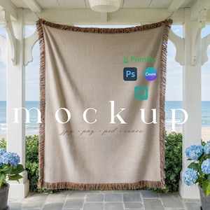 May include: A beige throw blanket with a fringed edge hangs from a porch. The word "mockup" is displayed in large white letters across the blanket. The blanket is hanging in front of a view of the ocean.