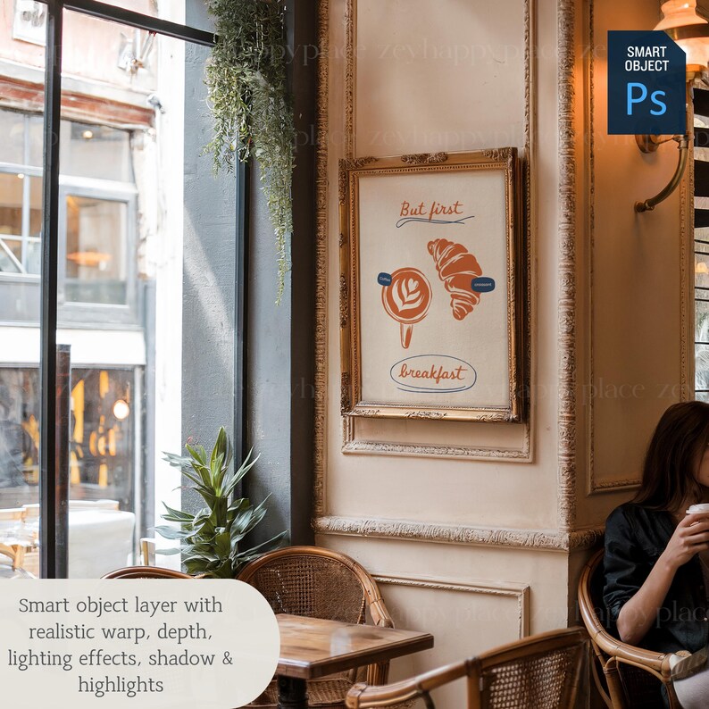 K&ouml;nnte beinhalten: Eine gerahmte Illustration eines Croissants und einer Tasse Kaffee mit dem Text "But first, breakfast". Die Illustration ist in einem goldenen Rahmen und h&auml;ngt an einer Wand in einem Caf&eacute;.