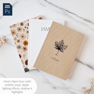 May include: Three notebooks with different covers are displayed on a white marble surface. One notebook has a floral pattern, another is plain white with the word "JAM" on it, and the third has a maple leaf illustration and the word "autumn".