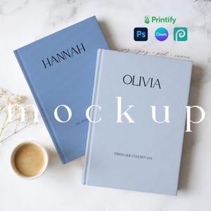 May include: Two hardcover books, one light blue and one periwinkle, with the names "HANNAH" and "OLIVIA" printed in black. The book on the right has the text "THINGS SHE COULDN'T SAY". A cup of coffee and sprigs of dried flowers are also visible.