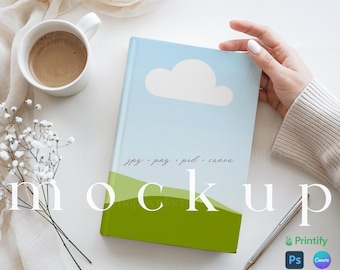 Può includere: Un mockup di libro blu e verde con una nuvola bianca sulla copertina. Il testo "jpg - png - psd - canva" è stampato sulla copertina. Il libro è su una superficie bianca con una tazza di caffè, una penna e fiori bianchi.