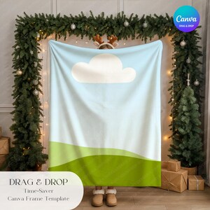 May include: A light blue blanket with a white cloud design and green hills at the bottom. The blanket is held up in front of a Christmas tree and garland. Text at the bottom reads "DRAG & DROP Time-Saver Canva Frame Template."