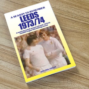 Puede incluir: Una portada de libro amarilla y blanca con el título "A Season to Remember Leeds 1973/74" y una foto de dos jugadores de fútbol con uniformes blancos. El texto debajo del título dice "A match by match account of Leeds 1973/74 Football League title-winning season with Neil Fissler."