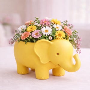 May include: A yellow elephant-shaped planter filled with a variety of colorful flowers. The flowers include white, yellow, pink, and orange daisies and other blooms. The planter is a cheerful decorative item.