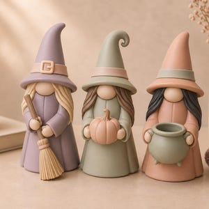 Peut inclure: Trois figurines de gnomes portant des chapeaux pointus et de longues robes. Le premier gnome tient un balai, le deuxième tient une petite citrouille et le troisième tient un chaudron. Ils sont colorés dans des tons sourds de violet, vert sauge et pêche.