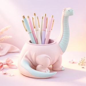 Puede incluir: Un portalápices rosa con forma de dinosaurio con detalles en azul claro, que contiene bolígrafos en colores pastel. Los bolígrafos son rosas, azules y blancos, con detalles dorados. El fondo es rosa suave. Accesorio de escritorio decorativo.