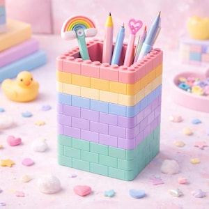 Op de afbeelding: Een pastelkleurige bureau-organizer gemaakt van gestapelde blokken, met pennen en een regenboog-topper gum. Een gele badeend en een hartvormige schaal gevuld met kleurrijke versieringen zijn ook zichtbaar, wat een speelse werkruimte creëert.