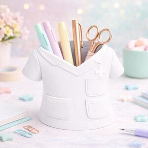 Peut inclure: Un organiseur de bureau blanc en forme de blouse d'infirmi&egrave;re, contenant des stylos et des ciseaux. Des stylos aux couleurs pastel, un stylo dor&eacute; et des ciseaux or rose sont visibles. D'autres accessoires de bureau sont pr&eacute;sents.