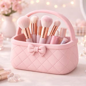 Könnte beinhalten: Ein rosa gesteppter Make-up-Pinselhalter mit Schleife, gefüllt mit Make-up-Pinseln und Schönheitsprodukten. Der Halter hat einen Griff und ist von anderen Schönheitsartikeln umgeben, darunter Parfüm und Lippenstifte.