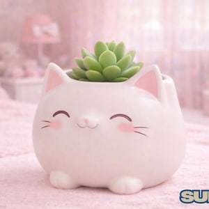 May include: A white ceramic cat-shaped planter with a smiling face, pink inner ears, and blush. It holds a green succulent plant. The planter sits on a pink surface, with a blurred pink background.