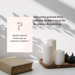 May include: A white card with a question mark and the text 'Quelles sont les choses qui me motivent vraiment?'  Three white candles on a wooden tray with three dark green figs. The text 'Ces cartes peuvent êtres utilisées en début ou en fin de séance de coaching.' is visible above the candles.