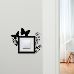 May include: Black decorative light switch cover with butterfly and floral accents. The cover features two butterflies, a flower, and foliage around a square frame. The switch itself is white.