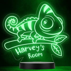 May include: Green neon night light shaped like a cartoon chameleon sitting on a branch with leaves. The light has the text "Harvey's Room" on it.