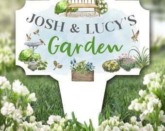 Può includere: Un cartello da giardino bianco con uno sfondo acquerellato blu. Il cartello dice "Josh & Lucy's Garden" con una panchina, fiori e uccelli illustrati su di esso.