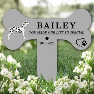 May include: A gray bone-shaped pet memorial with the name "BAILEY" and the text "YOU MADE OUR LIFE SO SPECIAL" with a heart and paw print. The dates "2010-2024" are below the text. A black and white dalmatian dog silhouette is on the left side of the bone.