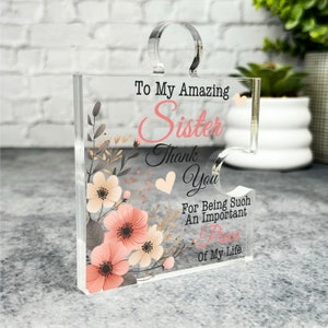 Puede incluir: Una pieza de rompecabezas de acrílico transparente con un diseño floral y el texto "To My Amazing Sister Thank You For Being Such An Important Piece Of My Life".