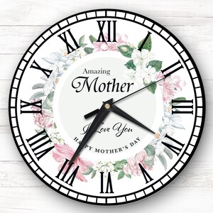 May include: White clock with black Roman numeral hour markers and black hands. The clock face has a floral design with pink and white flowers and green leaves. The text "Amazing Mother I Love You Happy Mother's Day" is printed on the clock face.
