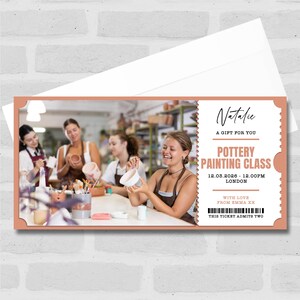 Puede incluir: Un vale de regalo para una clase de pintura de cerámica. El billete tiene un borde melocotón y presenta una foto de personas en un estudio de arte. El texto en el billete dice "Natalie, A Gift For You, Pottery Painting Class, 12.03.2026 - 12.00PM London, With Love From Emma XX, This Ticket Admits Two."