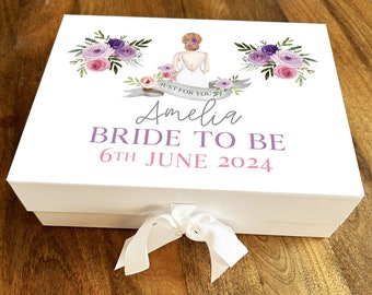 Pode incluir: Caixa de presente branca com um design floral roxo e rosa e uma silhueta de noiva. A caixa tem uma fita branca e o texto "Just for you Amelia Bride to be 6th June 2024".