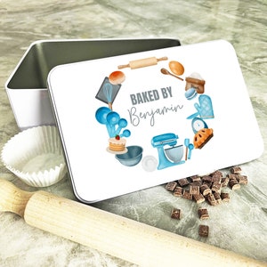 Puede incluir: Lata de metal blanca con una ilustración azul y blanca de herramientas para hornear y el texto "Baked by Benjamin".