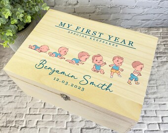 May include: A wooden keepsake box with a light wood finish and a teal inscription that reads "My First Year Special Keepsakes". The box features a series of illustrations of a baby boy growing from a newborn to a toddler. The box is personalized with the name "Benjamin Smith" and the date "12.03.2023".
